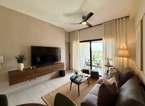 En moderne stue med et fladskærms-tv, en loftsvift, en sofa, et sofabord og udsigt til en balkon.