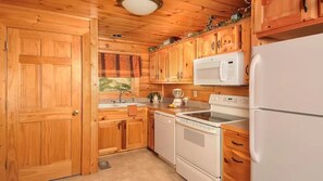 A wooden cabin-style kitchen with a white refrigerator, stove, microwave, and dishwasher. - A Walk In The Clouds, panoramic View (Sevierville)