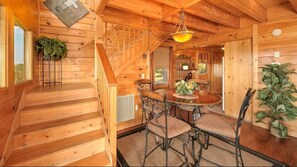 A wooden interior with a staircase, a dining area with a table and chairs, and a hanging light fixture. - A Walk In The Clouds, panoramic View (Sevierville)