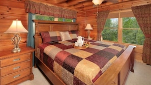 A wooden cabin bedroom with a bed, two bedside lamps, a dresser, and a window with curtains. - A Walk In The Clouds, panoramic View (Sevierville)