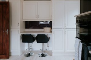 A compact kitchen with white cabinets, a black countertop, and two black bar stools. - Perfect Booking 3 Bed Home With Beautiful Garden (Ashford)