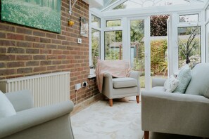 Une véranda avec un mur en briques, un radiateur, deux canapés et une vue sur le jardin.