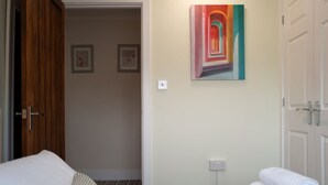 A hotel room with a bed, a painting on the wall, and a door leading to another room. - Perfect Booking 3 Bed Home With Beautiful Garden (Ashford)