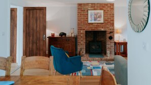 A living room with a brick fireplace, wooden furniture, and a blue armchair. - Perfect Booking 3 Bed Home With Beautiful Garden (Ashford)