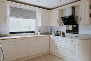 Une cuisine moderne avec des meubles blancs, une hotte noire et une fenêtre agrémentée d’une lambrequin à motifs.