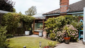 A residential garden with a lawn, potted plants, a wooden bench, and a brick chimney. - Perfect Booking 3 Bed Home With Beautiful Garden (Ashford)