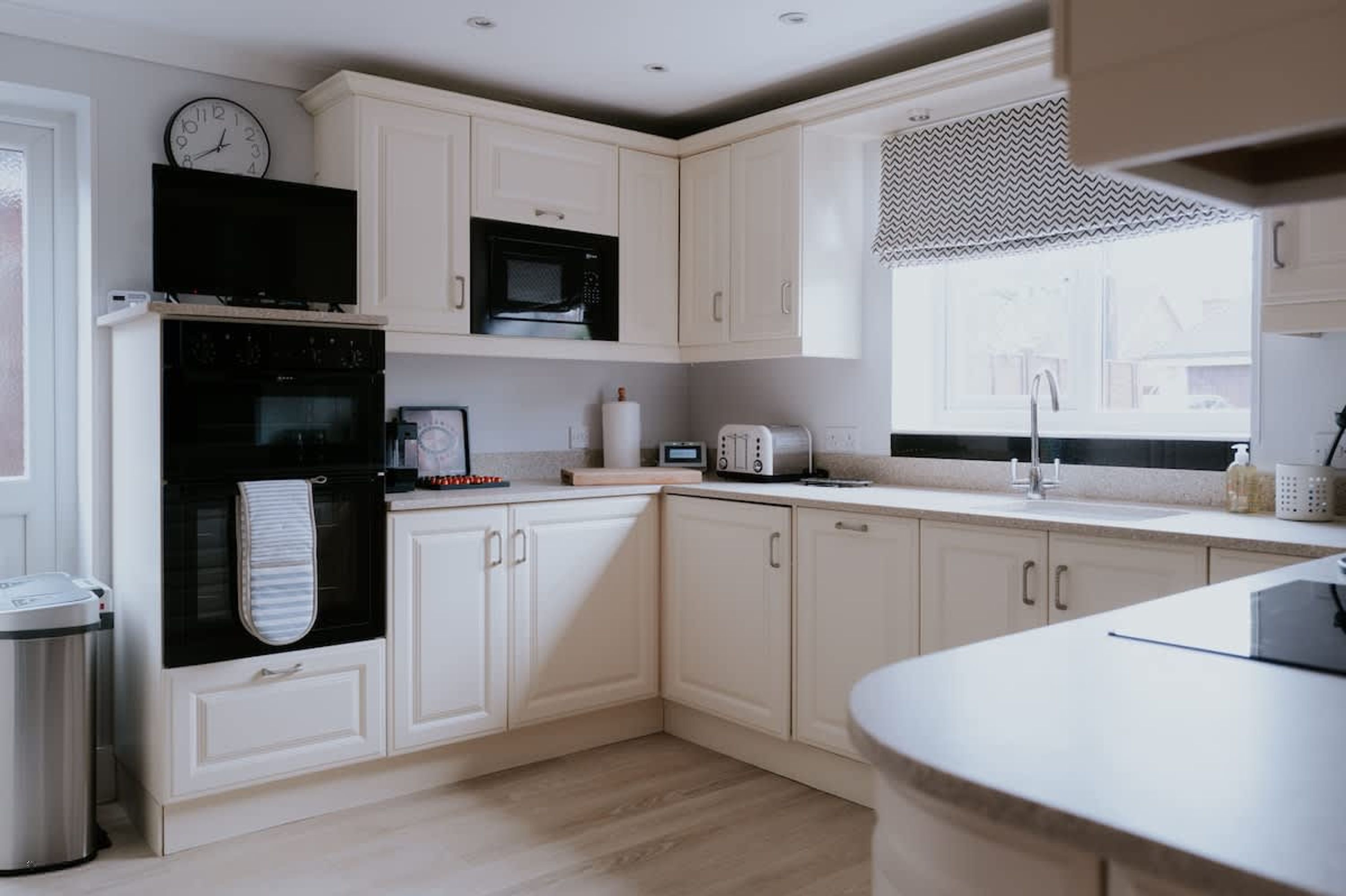 Una cucina moderna con mobili bianchi, un forno a microonde, un forno e una finestra con tenda decorata.