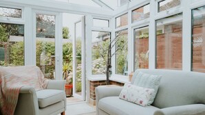 A conservatory with a sofa and armchair, large windows, and a view of the garden. - Perfect Booking 3 Bed Home With Beautiful Garden (Ashford)