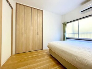 A bedroom with a wooden wardrobe, a bed, and a window with curtains. - LunaStay Apartments - 103 (東京)