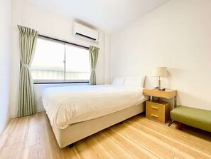 A hotel room with a bed, bedside table, lamp, and a bench. - LunaStay Apartments - 103 (東京)