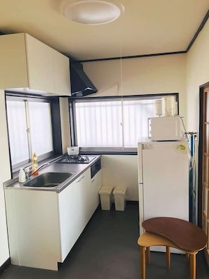 Eine kleine Küche mit Spüle, Herd und Kühlschrank, ein Fenster mit Jalousien und ein Stuhl.