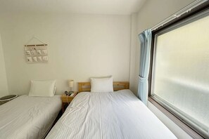 Ein Hotelzimmer mit zwei Betten, einem Nachttisch mit Lampe, einem Kalender und einem großen Fenster mit Vorhängen.