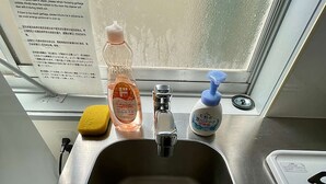 En diskho i rostfritt stål med en gul svamp, en flaska flytande tvål och en blå pumpflaska.