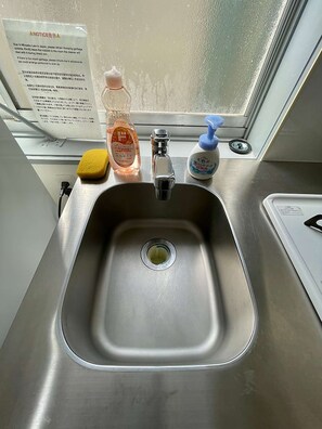 A stainless steel sink with a yellow sponge, a bottle of liquid soap, and a blue pump bottle. - LunaStay Apartments - 203 (東京)