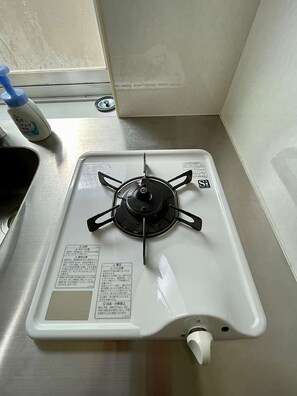 A white gas stove with four burners, a control panel, and a white control knob. - LunaStay Apartments - 203 (東京)