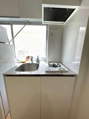 A compact kitchen with a sink, a gas stove, and a window providing natural light. - LunaStay Apartments - 203 (東京)