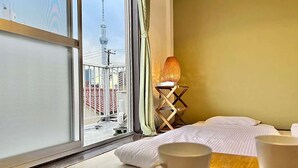 Een hotelkamer met een groot raam, een bed, een nachtkastje met twee bekers, en een lamp.
