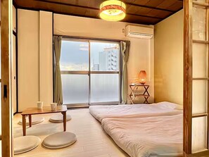 A room with a bed, a table, a lamp, and a view of the city through a large window. - LunaStay Apartments - 302 (東京)
