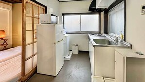 Een kleine keuken met een koelkast, magnetron, spoelbak en raam.
