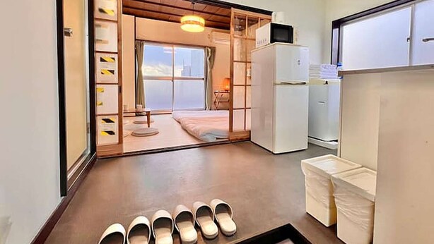 Een hotelkamer met een schuifdeur naar een balkon, een koelkast en een paar slippers op de vloer.