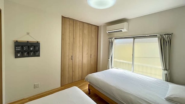 Un dormitorio con dos camas, un armario de madera, aire acondicionado de pared y un calendario.
