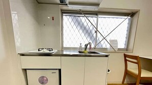 Una cocina pequeña con ventana, un refrigerador compacto y una silla de madera.