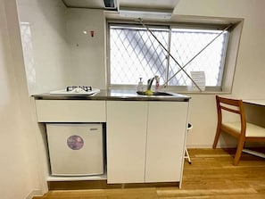 Eine kleine Küche mit Fenster, einem Kühlschrank und einem Holzbstuhl.