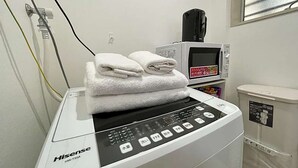 Un electrodoméstico HiseSense HW-TS54 blanco con pantalla digital, un microondas y un cubo de basura en una habitación con ventana.