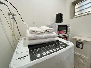 Ein weißes HiseSense HW-TS54 Gerät mit Digitalanzeige, einer Mikrowelle und einem Mülleimer in einem Zimmer mit einem Fenster.