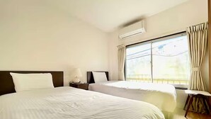 Quarto de hotel com duas camas, uma janela com cortinas, um ar condicionado e uma mesa de cabeceira com luminária.