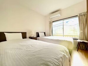 Ein Hotelzimmer mit zwei Betten, einem Fenster mit Vorhängen, einer Klimaanlage und einem Nachttisch mit Lampe.
