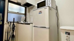Uma cozinha compacta com geladeira branca, micro-ondas e uma pequena janela.