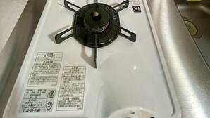 Um fogão a gás com superfície branca, painel de controle com instruções e um recipiente amarelo com tampa branca.