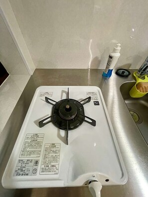 Ein Gaskochfeld mit weißer Oberfläche, einer Bedienblende mit Anweisungen und einem gelben Behälter mit weißem Deckel.