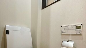 Sanita branca com autoclismo, suporte para papel higiénico e painel de controlo fixado na parede, num quarto de banho.