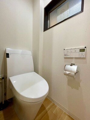Eine weiße Toilette mit Tank, Toilettenpapierhalter und einer an der Wand montierten Bedienkonsole im Badezimmer.