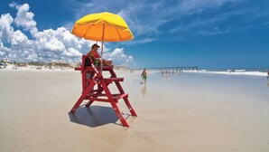 En livredderstand med en gul parasol på en sandstrand.