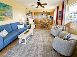 Ein Wohnzimmer mit einem blauen Sofa, einem grauen Sessel, einem Couchtisch und einem Essbereich mit Tisch und Stühlen.
