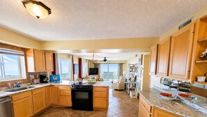 A spacious kitchen with wooden cabinets, a central island, and a dining area with a view. - Beachfront Ocean-Views Condo, Balcony! Pool, BBQ (St. Augustine Beach)