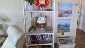 A white metal shelf unit with decorative items, books, and a small white cabinet with blue patterns. - Beachfront Ocean-Views Condo, Balcony! Pool, BBQ (St. Augustine Beach)