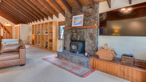 A cozy living room with a stone fireplace, wooden beams, a leather sofa, and a bookshelf. - Cozy Sunriver Retreat, 6 SHARC, AC, Loft & Wood Stove (Sunriver)