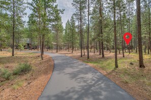 A forested area with a paved path, tall pine trees, and a building in the background. - Cozy Sunriver Retreat, 6 SHARC, AC, Loft & Wood Stove (Sunriver)