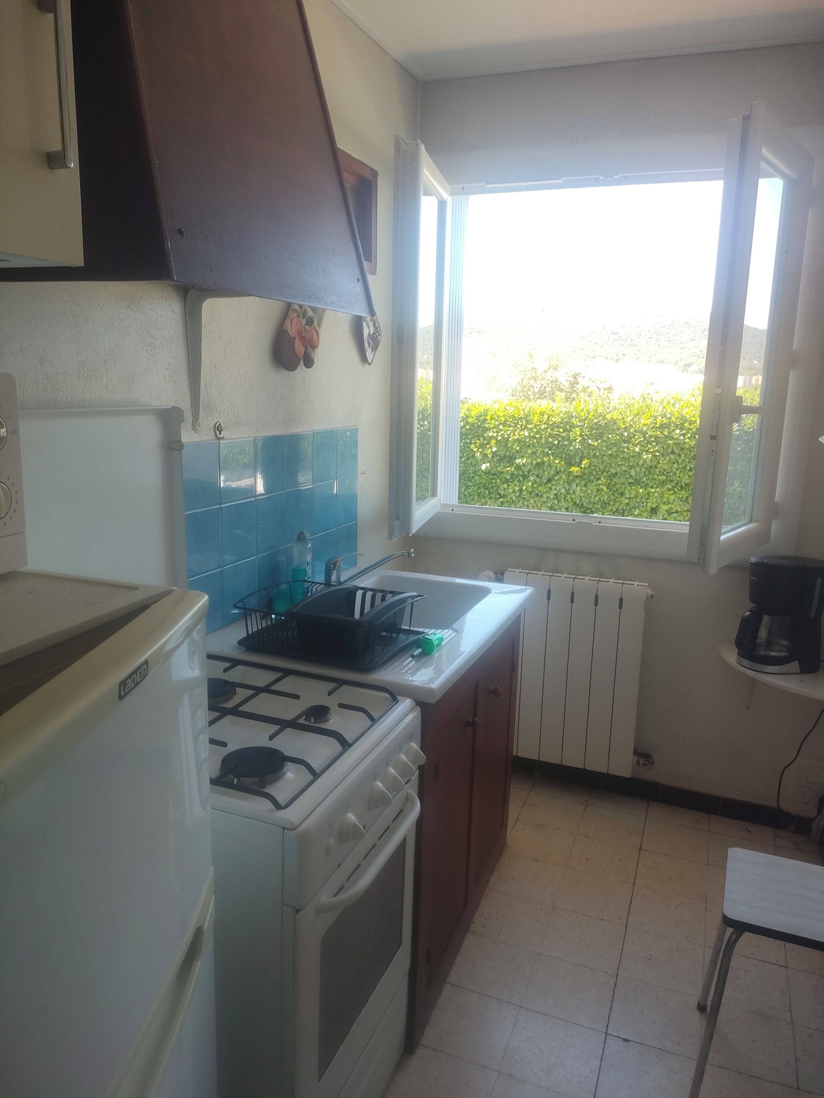 Une cuisine équipée d’une cuisinière à gaz, d’un évier et d’une fenêtre donnant sur un espace verdoyant.
