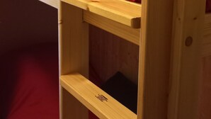 Ein Stockbett mit roter Matratze, einem Holz-Kopfteil und einem Regal.