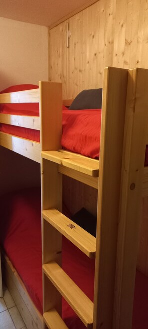 A bunk bed with a red mattress, wooden headboard, and a shelf unit. - Apartment for 2 to 6 people at the base of the slopes (Saint-Jean-d'Aulps)
