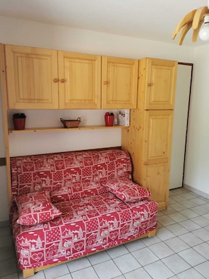 A room with a wooden cabinet, a red patterned sofa, and a tiled floor. - Apartment for 2 to 6 people at the base of the slopes (Saint-Jean-d'Aulps)