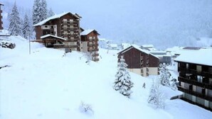 Ein verschneites Bergdorf mit Holzhäusern und einer Skipiste.