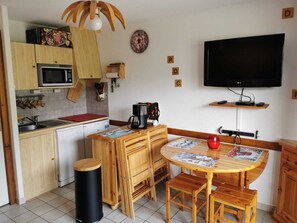A compact kitchen with a microwave, sink, and wooden cabinets. There's a dining table with chairs and a black trash bin. A flat-screen TV is mounted on the wall. - Apartment for 2 to 6 people at the base of the slopes (Saint-Jean-d'Aulps)