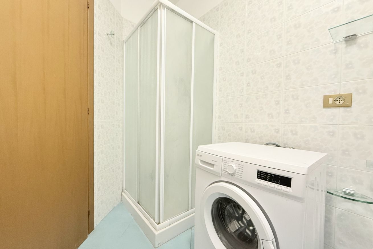 A bathroom with a shower, a washing machine, and patterned tiles.