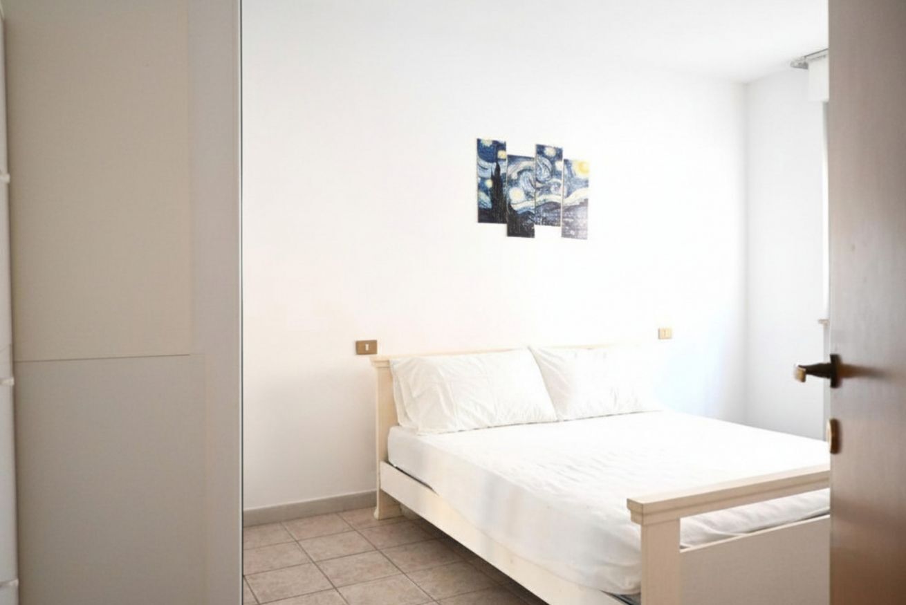 Ein Schlafzimmer mit einem Bett, weißen Wänden und einem kleinen Bild an der Wand.